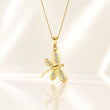 A gold dragonfly pendant necklace adorned with small clear crystals, displayed on a soft, light beige satin background with a subtle reflection below. – Aurelia Dragonfly Lab-Grown Diamond Pendant