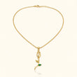 A delicate gold chain necklace with a pendant featuring a small green leaf and a clear crystal, displayed on a light cream background. – Emerald Rose Pendant Necklace