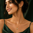 A woman wearing a delicate gold chain necklace with a diamond-shaped pendant featuring a central clear gemstone, styled with a dark green satin top against a dark background. – Geometric Spark Diamond Pendant Necklace