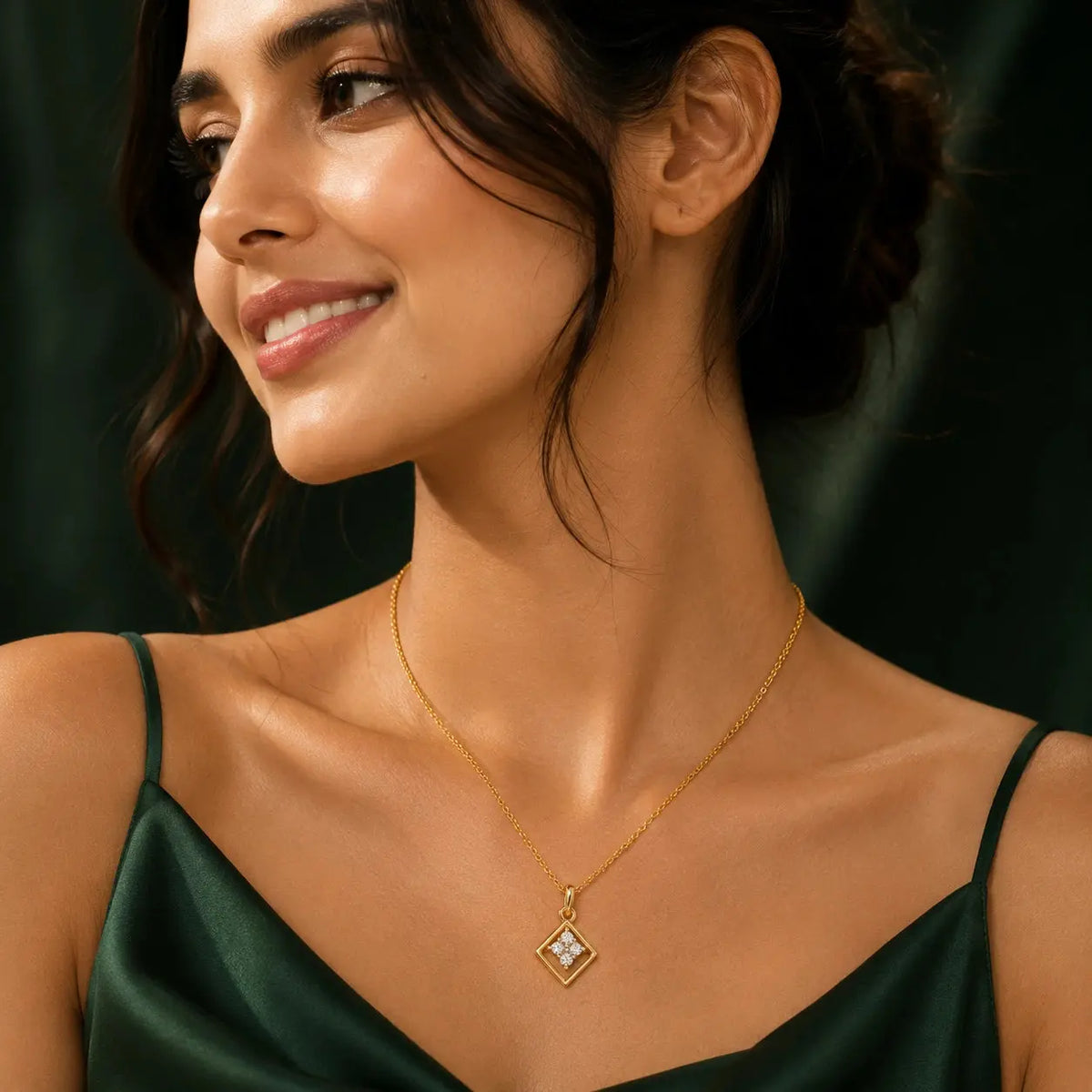 A woman wearing a delicate gold chain necklace with a diamond-shaped pendant featuring a central clear gemstone, styled with a dark green satin top against a dark background. – Geometric Spark Diamond Pendant Necklace